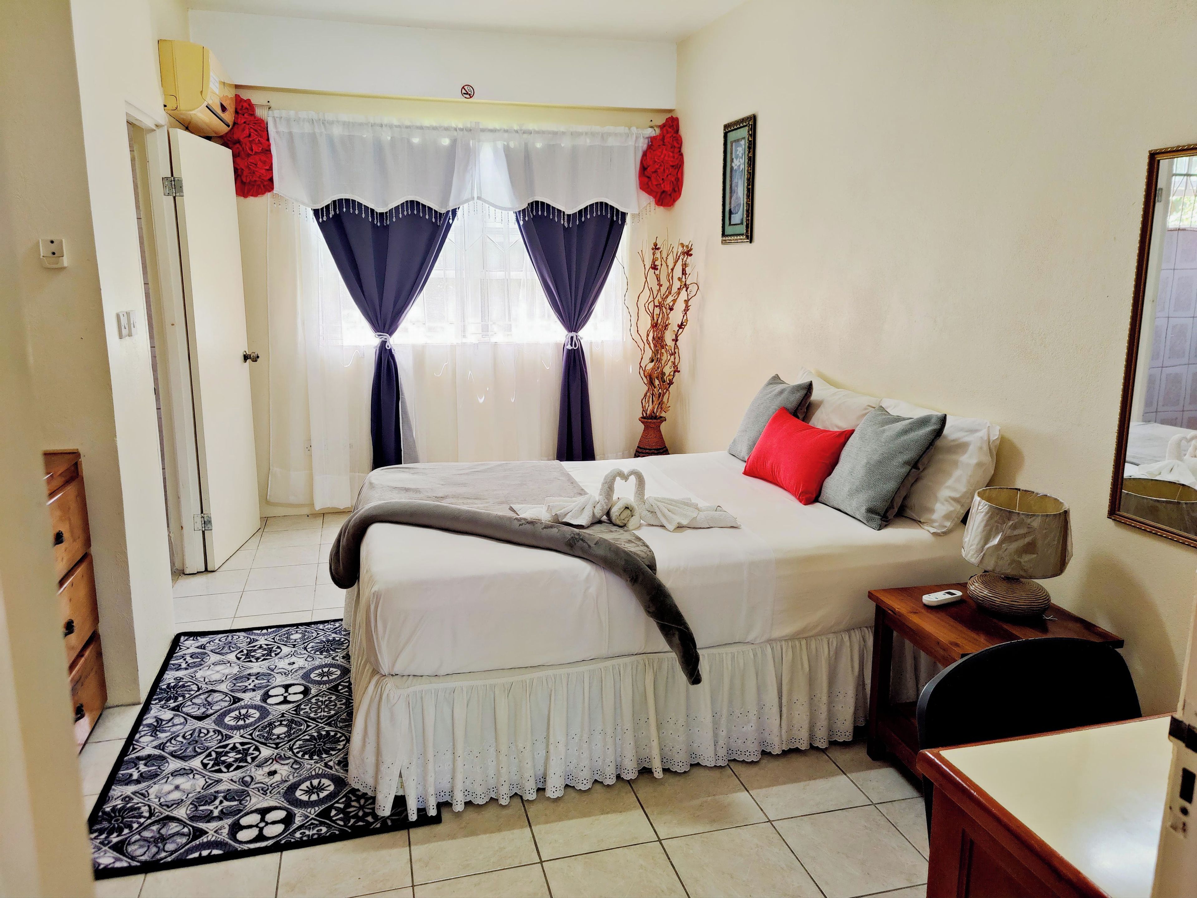 A bedroom with a bed, bedside table, lamp, and a window with curtains.