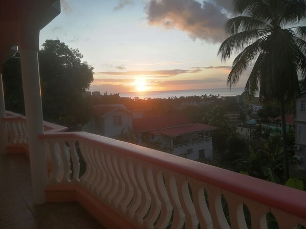 A balcony with a railing overlooking a sunset view of a coastal town.