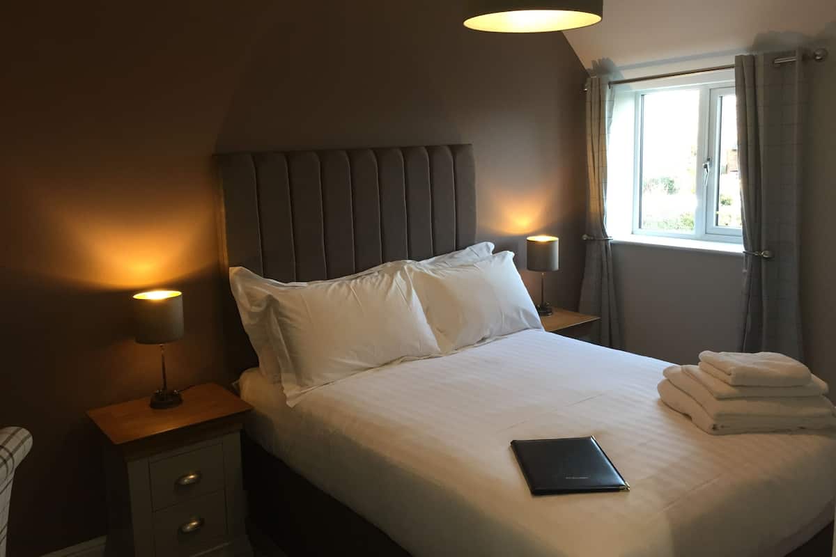 A neatly made bed with white linens, a bedside lamp, and a laptop on the bed.