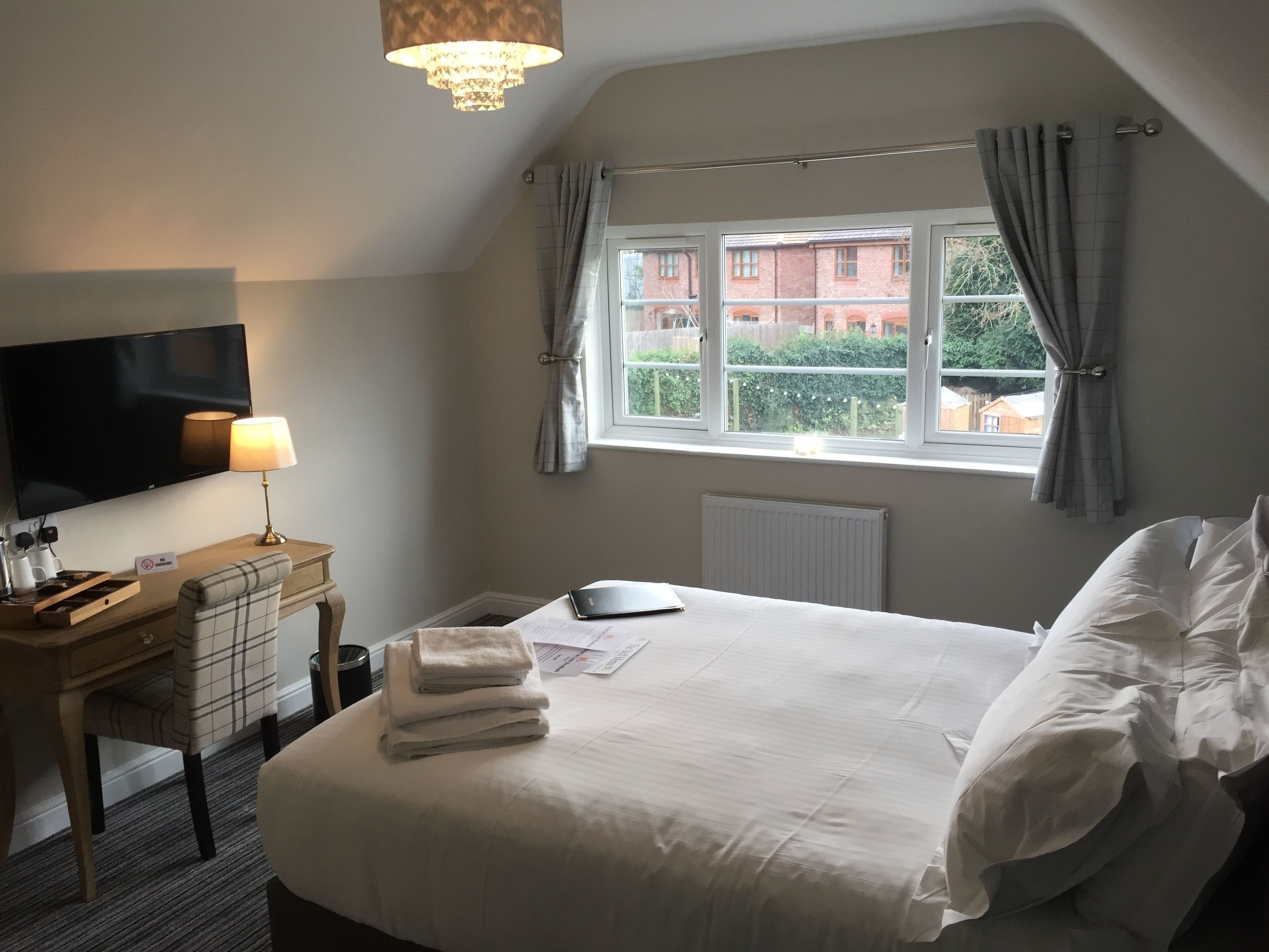 Una habitación de hotel con cama, escritorio con lámpara, televisión y ventana con cortinas.