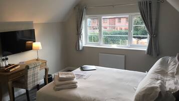 Una habitación de hotel con cama, escritorio con lámpara, televisión y ventana con cortinas.