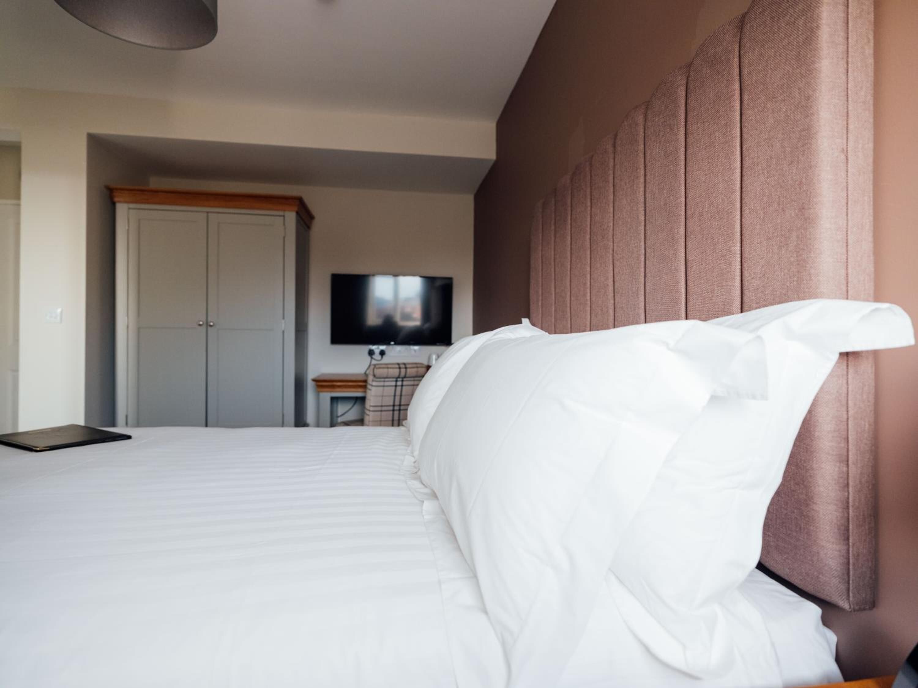 A hotel room with a large bed, a television on the wall, a desk, and a wardrobe.
