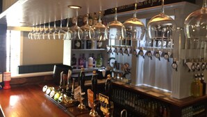Een bar met verschillende biertaps, een keuze uit flessen en hangende wijnglazen.