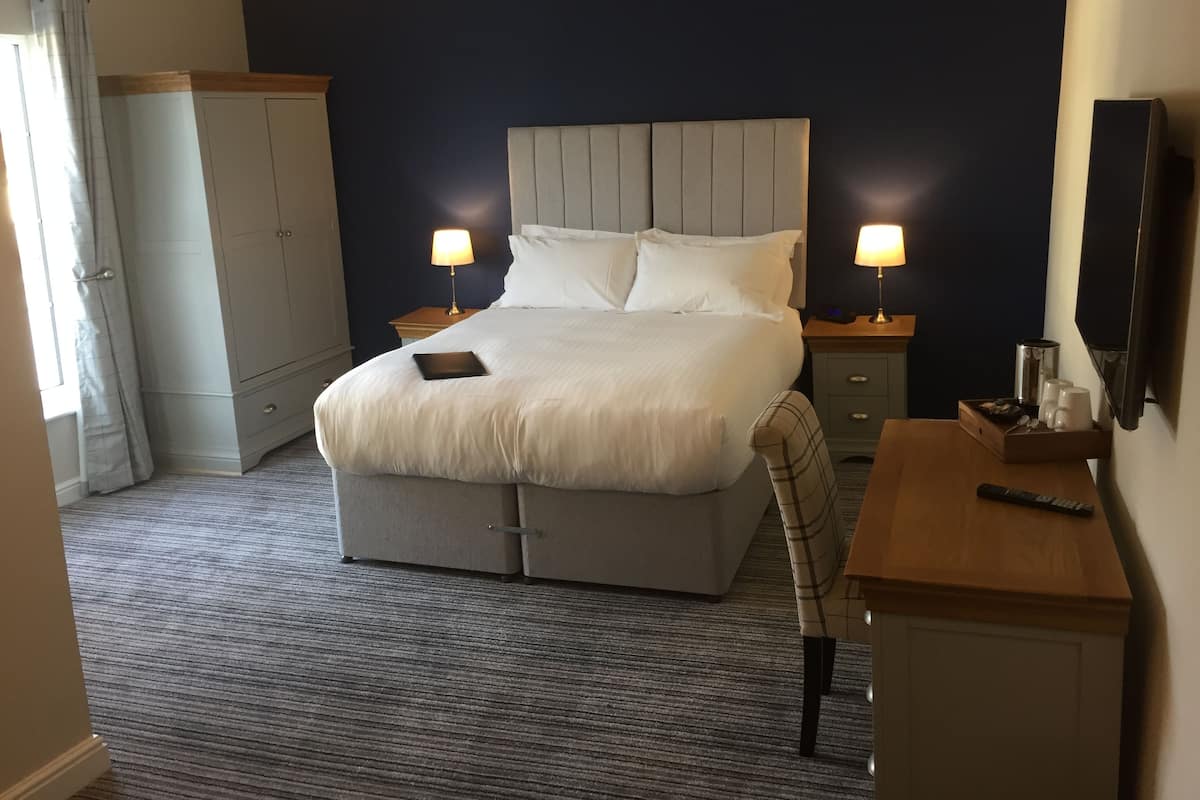 A hotel room with a large bed, bedside tables, a desk, a chair, a wardrobe, and a television.
