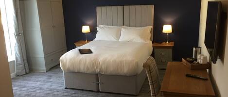 Une chambre d’hôtel avec un grand lit, des tables de chevet, un bureau, une chaise, une armoire et un téléviseur.