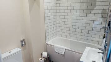 Un baño con inodoro blanco, lavamanos blanco y bañera con ducha.