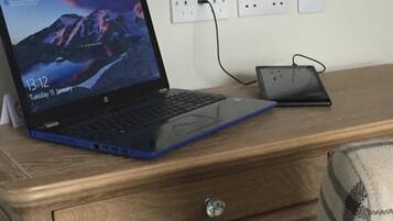 A laptop on a wooden desk with a power strip and a phone charger.