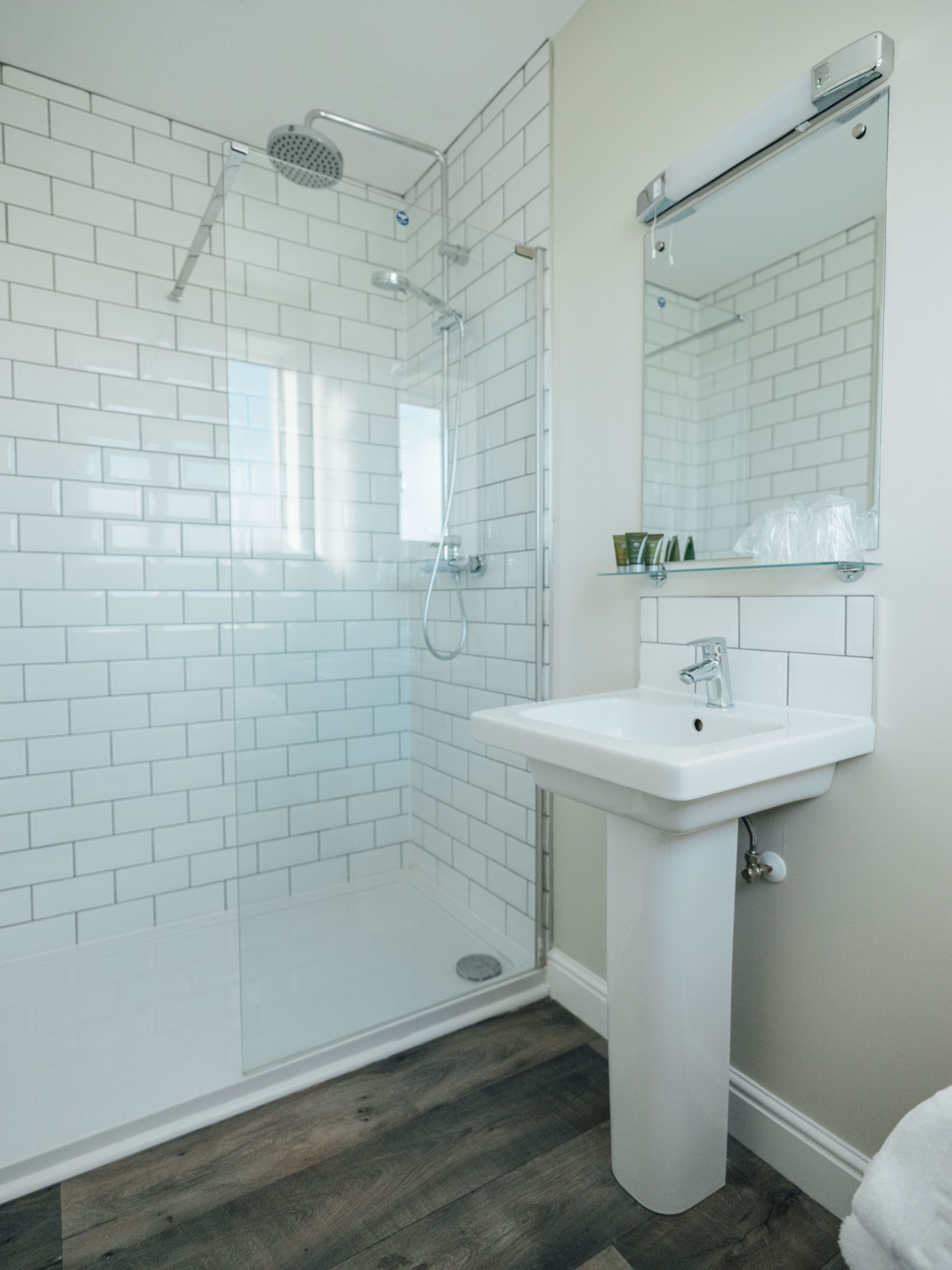 A bathroom with white subway tiles, a glass shower enclosure, a white sink, and a mirror above it.