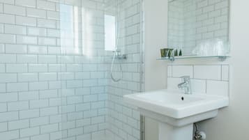 A bathroom with white subway tiles, a glass shower enclosure, a white sink, and a mirror above it.
