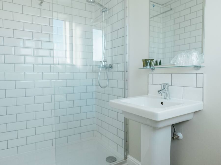A bathroom with white subway tiles, a glass shower enclosure, a white sink, and a mirror above it.