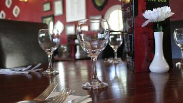 Una mesa de comedor con copas de vino vacías, cubiertos y un atril para el menú.