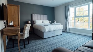 Een moderne hotelkamer met een groot bed, een bureau met stoel, een kledingkast en een groot raam met gordijnen.