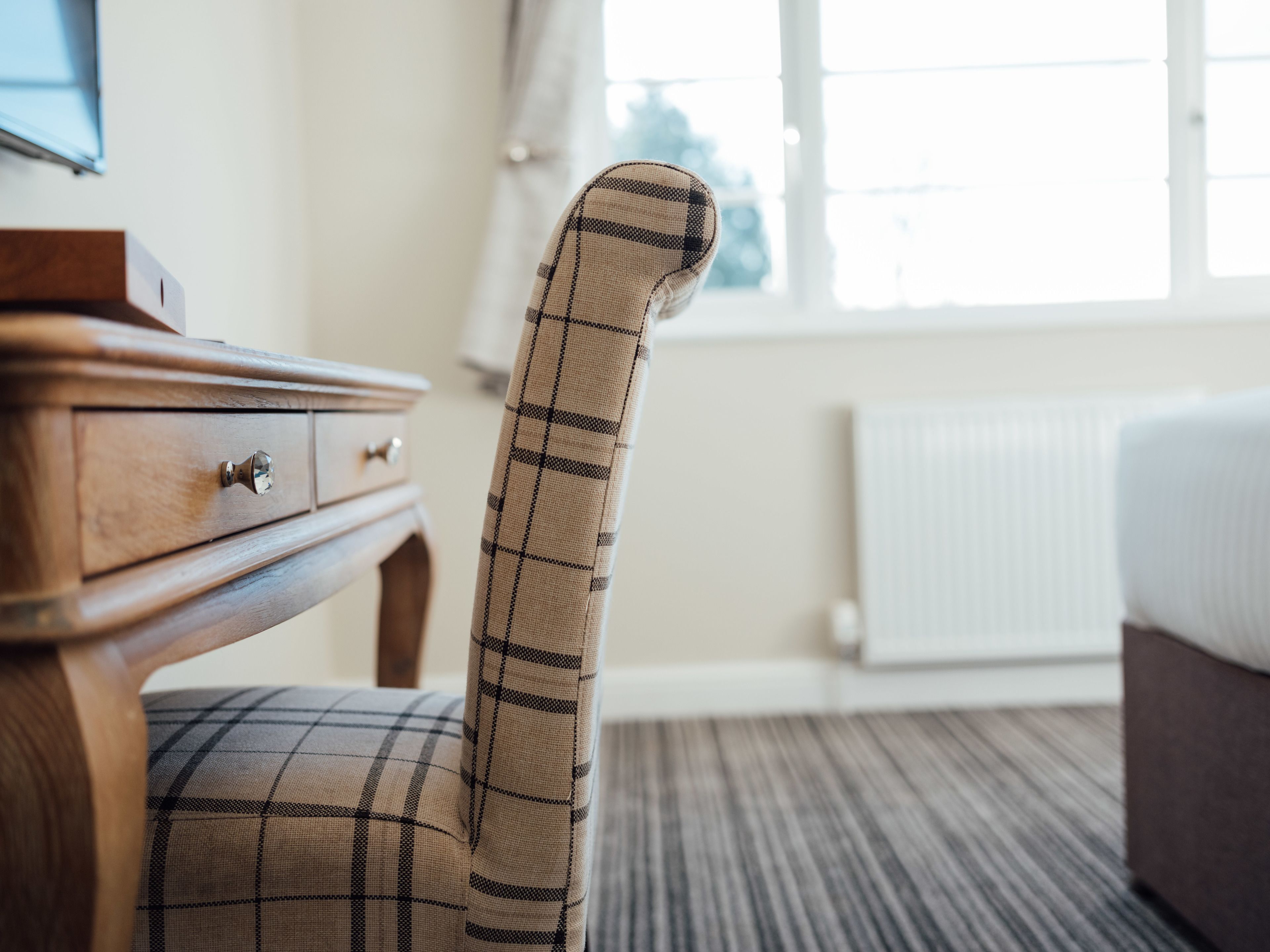 A plaid-patterned chair in a hotel room with a wooden dresser and a radiator.