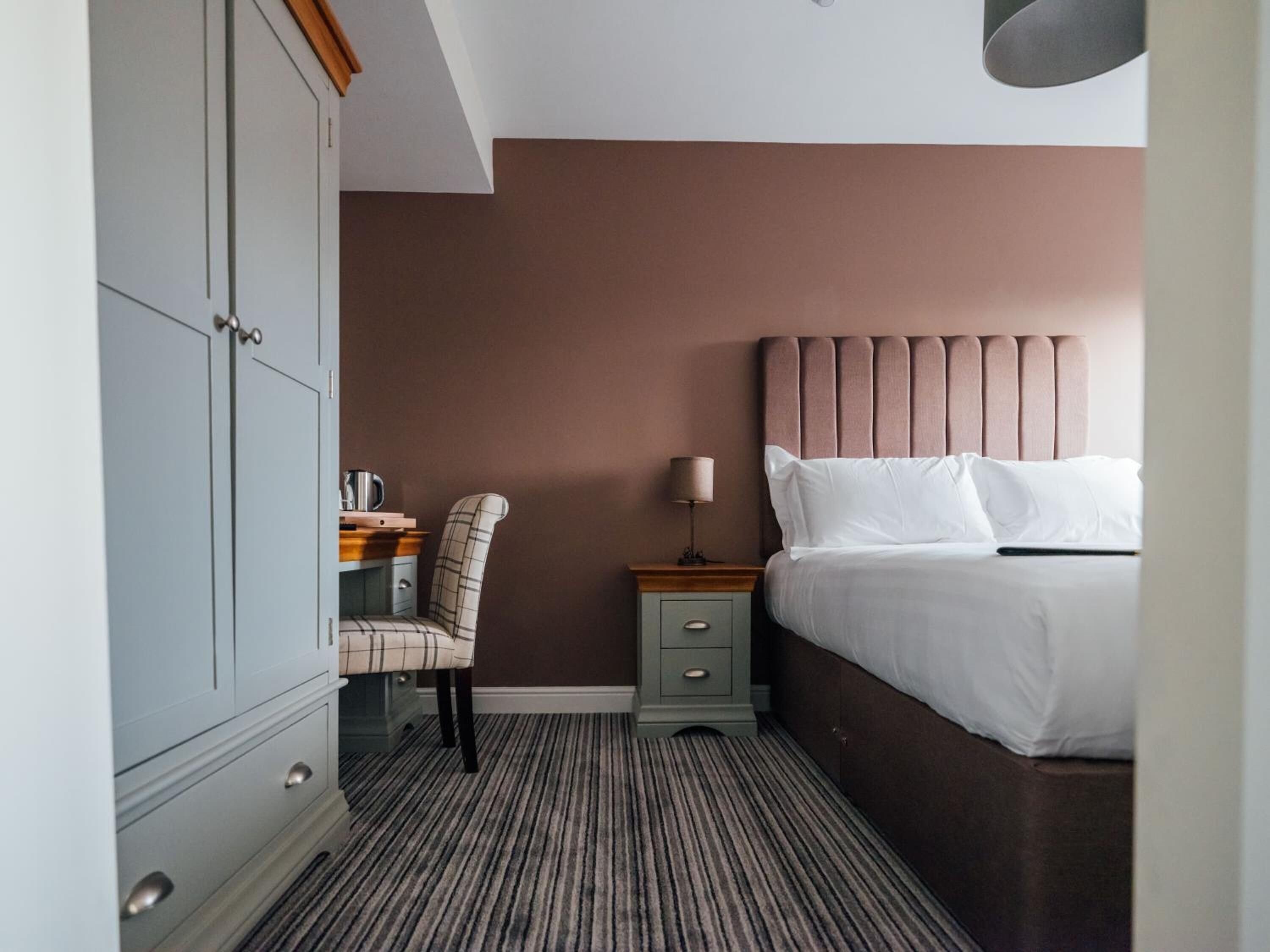 A hotel room with a bed, a desk with a chair, a nightstand, and a wardrobe.
