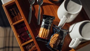 A wooden tray with a packet of biscuits, two spoons, two white cups, and a small box of chocolates.