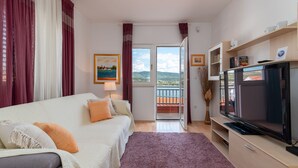 A bedroom with a bed, a TV, a window with a view of the countryside, and a door leading to a balcony. - Mandic Apartment - Seaside Views, Beach Nearby (Mastrinka)