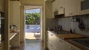 A kitchen with white cabinets, a wooden countertop, and a view to an outdoor area with a tiled patio and greenery. - Dimora dei Giganti - a typical neapolitan terrace (Napoli)