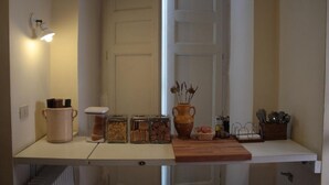 A kitchen with a white countertop, jars of food, a vase with dried plants, and a hanging light fixture. - Dimora dei Giganti - a typical neapolitan terrace (Napoli)