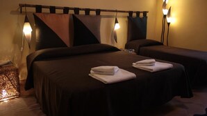 A hotel room with two beds, each with a dark-colored bedspread and pillows. There are two bedside lamps, a decorative wall piece above the beds, and a small table with a lamp and a box. - Dimora dei Giganti - a typical neapolitan terrace (Napoli)