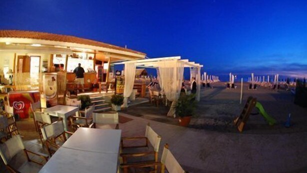 Un restaurante al aire libre con mesas y sillas, una zona de estar cubierta y vistas a la playa.