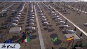 Una playa con hileras de sombrillas y banderas, lo que indica una disposición organizada para los bañistas.