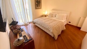 Un dormitorio con una cama grande, una mesita de noche, una lámpara y una ventana con cortinas.