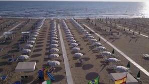 Een strand met rijen parasols en vlaggen, wat een georganiseerde indeling voor strandbezoekers aangeeft.
