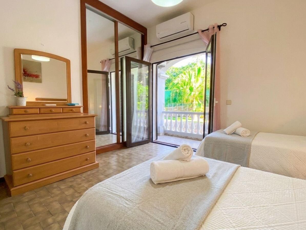 Een hotelkamer met een bed, een houten dressoir, een spiegel en een schuifdeur naar een balkon met uitzicht op groen.