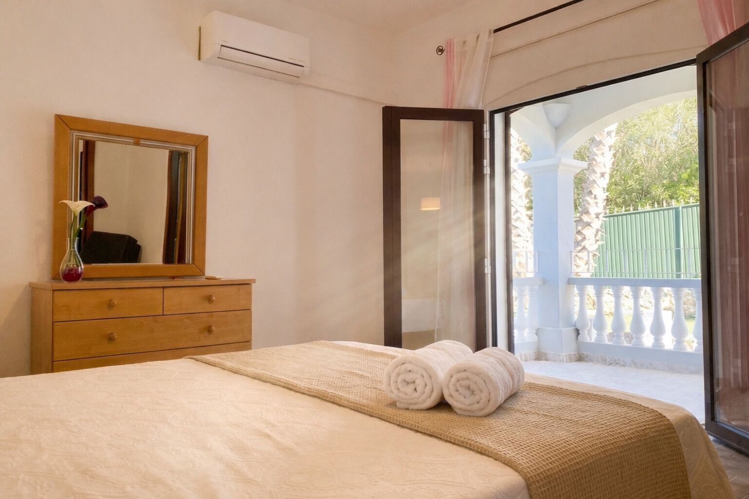 A hotel room with a bed, a dresser, a mirror, and a view of a balcony.