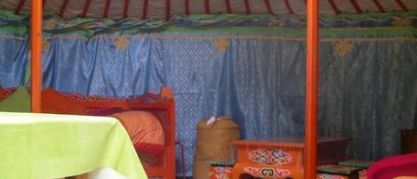 Interior de una yurtas tradicional con una cama, una mesa y un taburete pequeño.