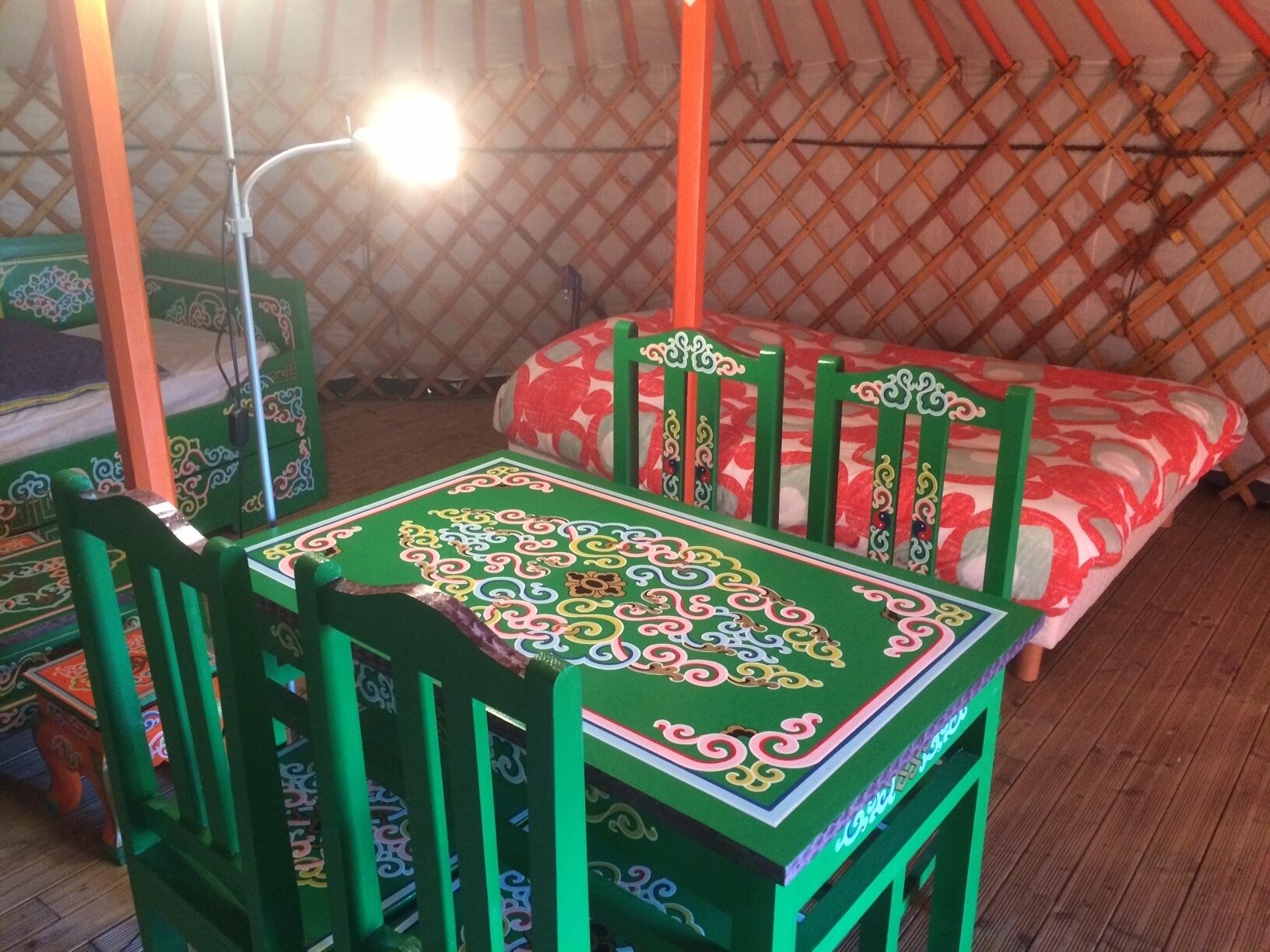 A room with a green and red patterned bed, a green table with intricate designs, and a wooden lattice wall.