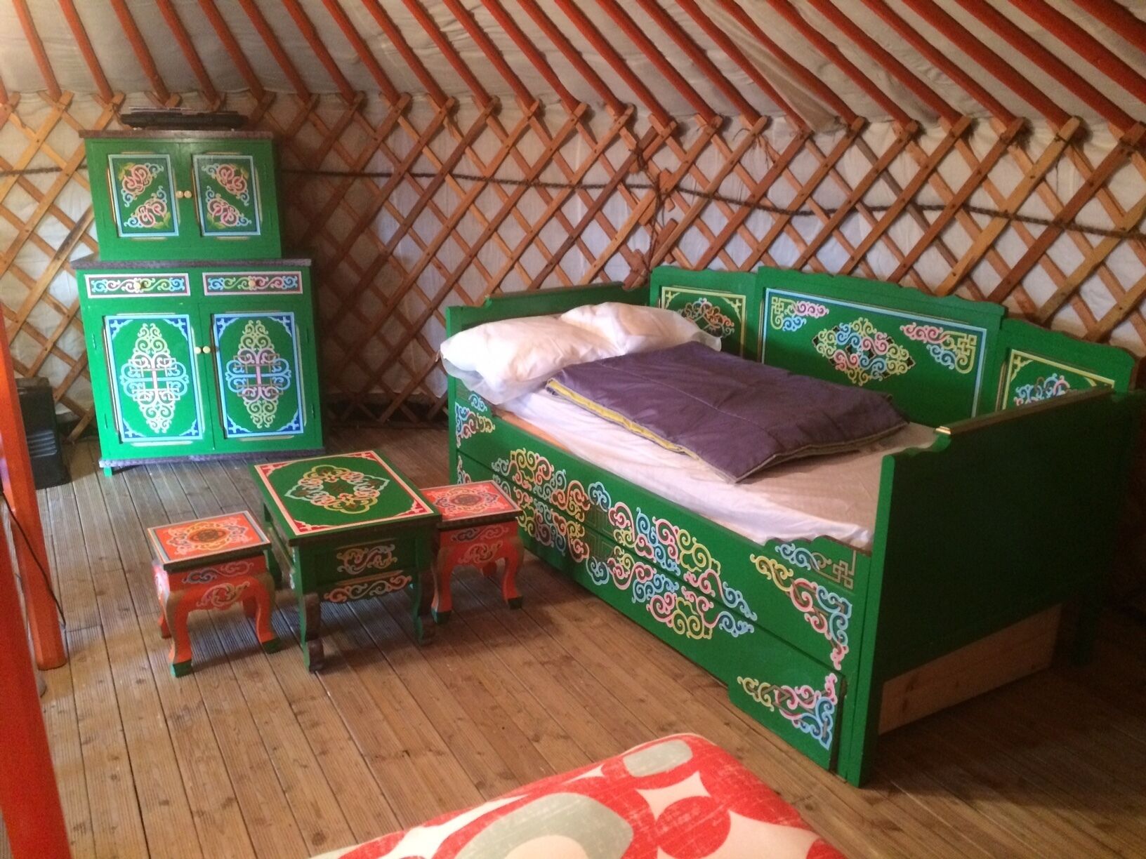 Une yourte traditionnelle avec un lit vert, des boîtes de rangement colorées et un plancher en bois.