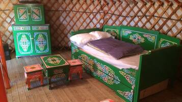 Une yourte traditionnelle avec un lit vert, des boîtes de rangement colorées et un plancher en bois.