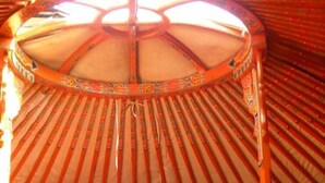 A traditional yurt interior with a bed, a table, and a lamp.