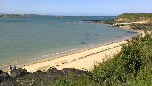 A coastal beach with clear waters, rocky outcrops, and a sandy shoreline.