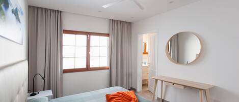 A modern bedroom with a bed, a desk, a ceiling fan, and a large window with curtains.