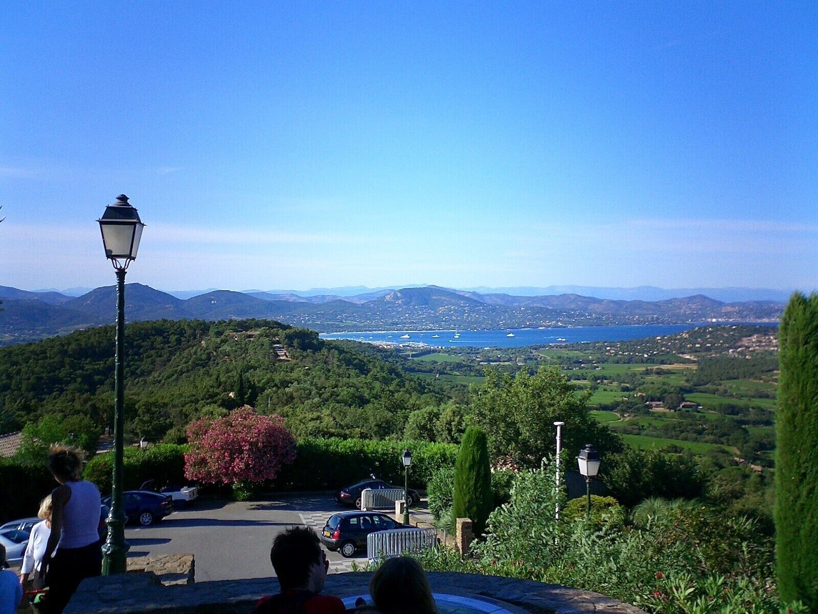 Une vue panoramique depuis le sommet d’une colline, avec un espace de stationnement, un lampadaire et une étendue d’eau visible au loin.