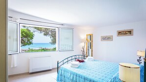 Un dormitorio con cama, ventana con vista al mar, radiador y lámpara.