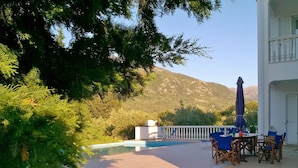 A poolside area with a table and chairs, a pool, and a mountain view.