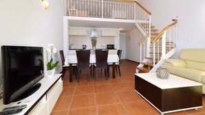 Un salon spacieux équipé d’un téléviseur à écran plat, d’une table à manger et de chaises. Un escalier mène à l’étage supérieur.