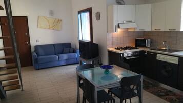Un espace de vie compact comprenant un coin cuisine, un canapé, une table à manger avec des chaises et un téléviseur.