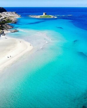 Vista aérea de una zona costera con aguas turquesas cristalinas, una playa arenosa y una pequeña isla con una estructura.
