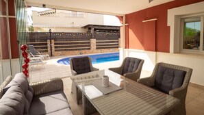 An outdoor patio area with wicker furniture, a pool, and a view of a building in the background. - Stunning Villa - Open Plan & Heated 8m Pool  (Torre-Pacheco)