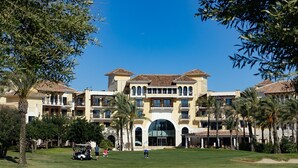 A large, multi-story hotel with a central courtyard, palm trees, and a golf course. - Stunning Villa - Open Plan & Heated 8m Pool  (Torre-Pacheco)