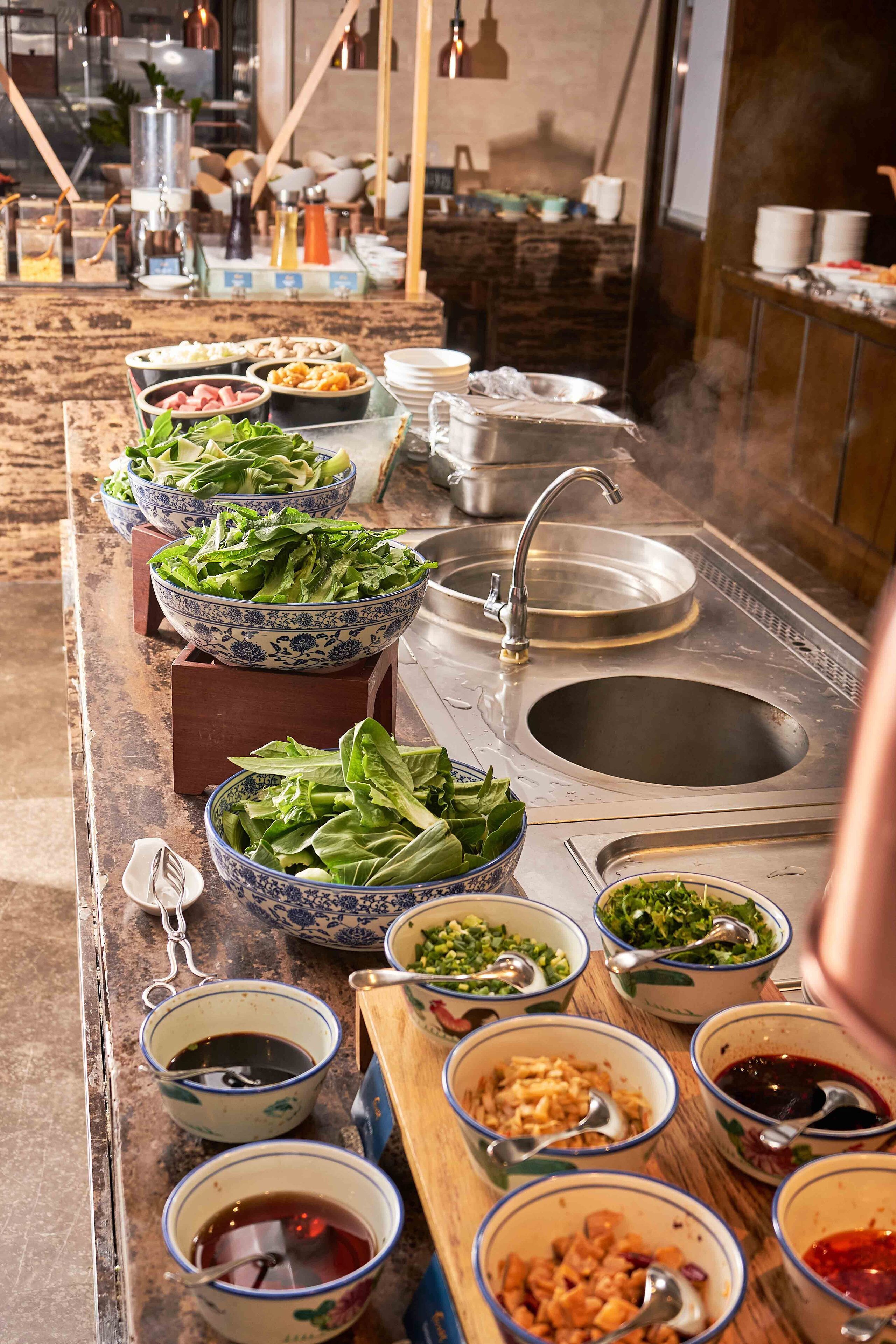 A buffet setup with various dishes and bowls, a sink, and a stove in the background.