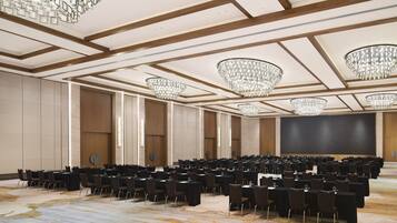 Un salón de conferencias con mesas y sillas en filas, grandes candelabros y un escenario.