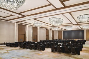 Un salón de conferencias con mesas y sillas en filas, grandes candelabros y un escenario.