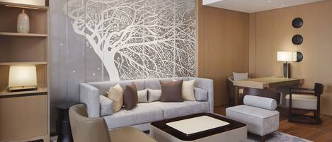 A modern living room with a grey sofa, a small ottoman, a coffee table, and a decorative tree mural on the wall.
