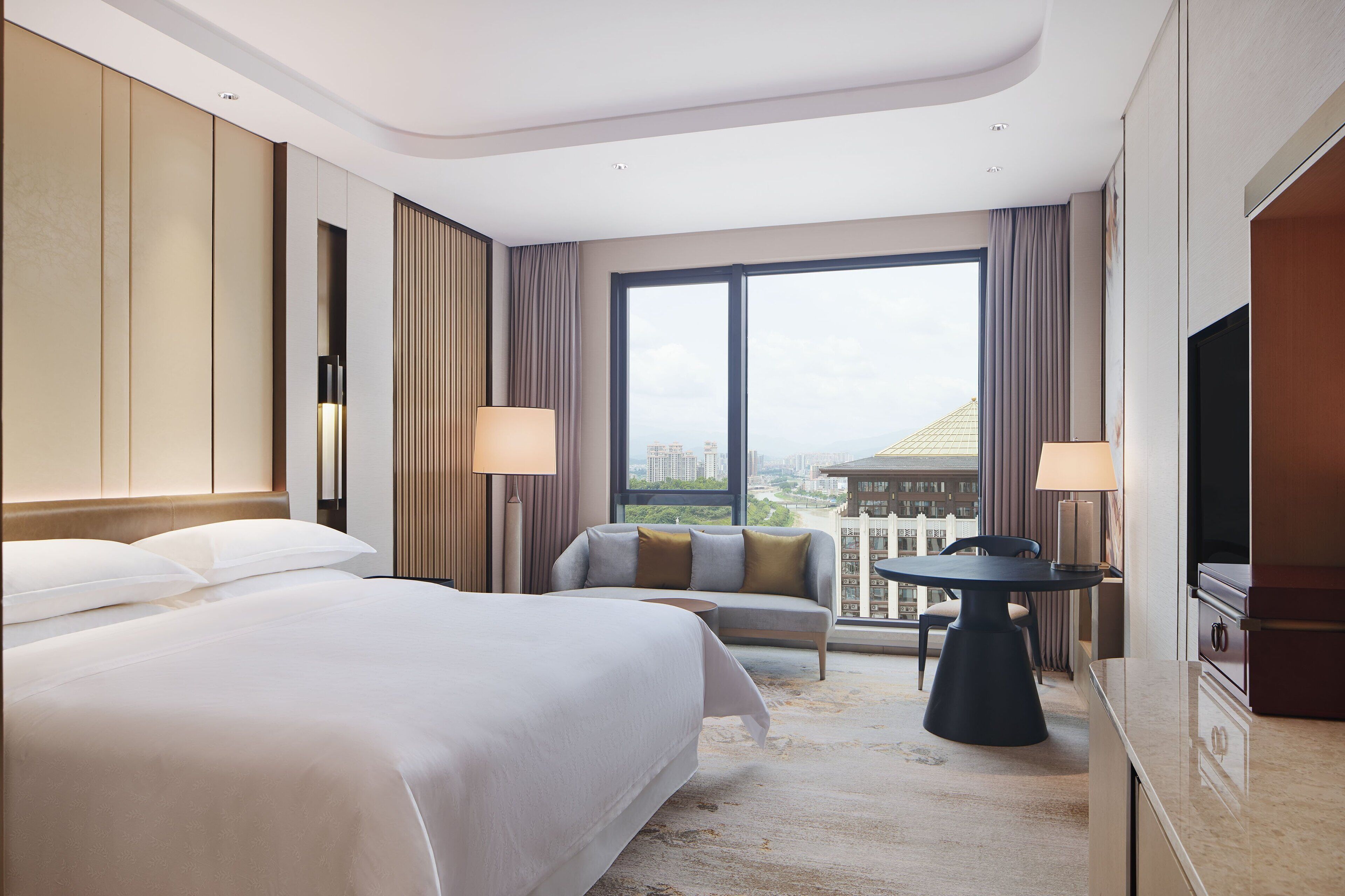 Una habitación de hotel con una cama grande, un sofá, una mesita y un televisor.