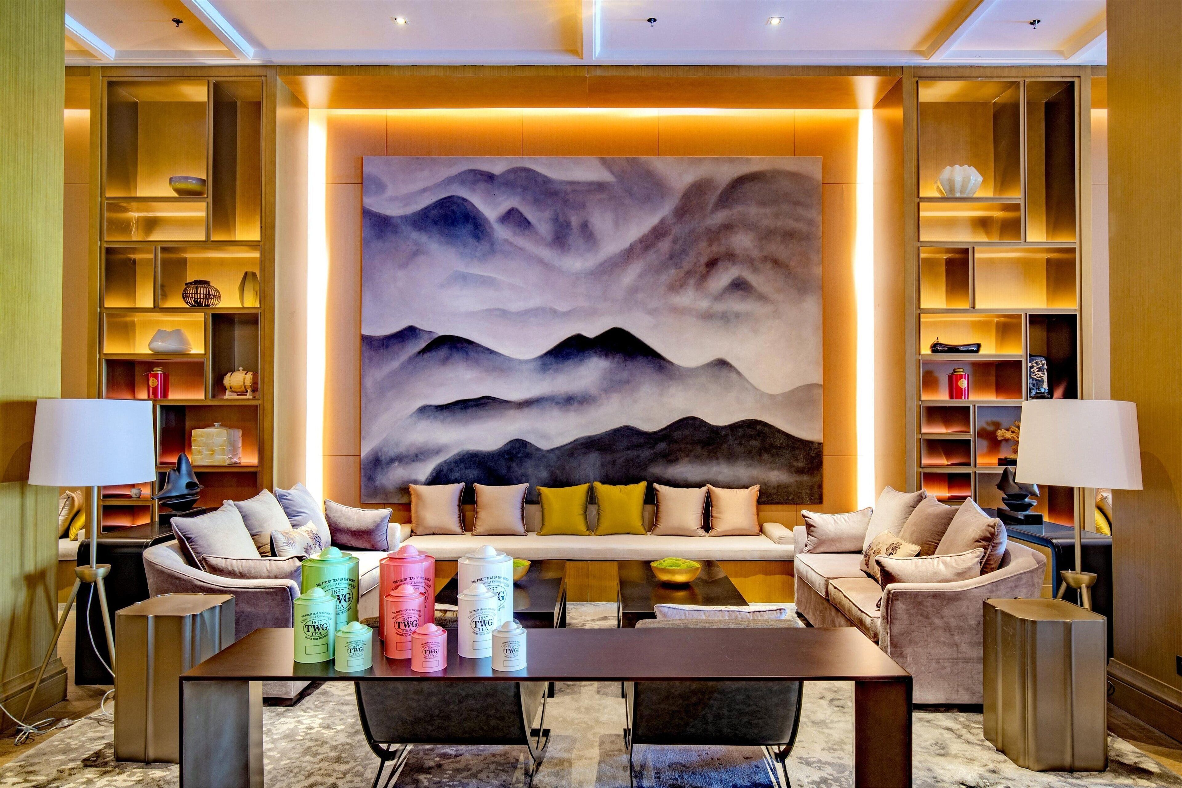 A modern living room with a sofa set, a coffee table with skincare products, and a large wall painting.